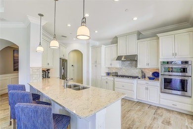 Kitchen featuring arched walkways, ornamental molding, a kitchen breakfast bar, a peninsula, and light stone counters