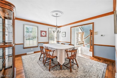 Dining space featuring light wood flooring, crown molding, a chandelier, and stairs