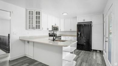 Kitchen with stainless steel appliances, wood finished floors, glass insert cabinets, white cabinetry, and a peninsula