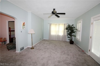 Carpeted spare room featuring ceiling fan, arched walkways, and baseboards