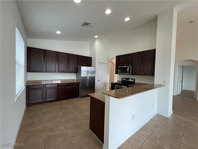 Kitchen with arched walkways, light tile patterned floors, dark brown cabinets, appliances with stainless steel finishes, and recessed lighting