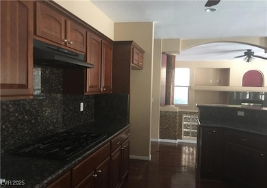 Kitchen with under cabinet range hood, black cooktop, ceiling fan, arched walkways, and decorative backsplash
