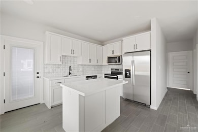 Kitchen with stainless steel appliances, decorative backsplash, light countertops, and white cabinetry