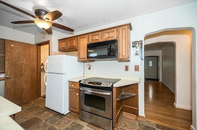 Kitchen with stainless steel electric range oven, arched walkways, light countertops, black microwave, and freestanding refrigerator