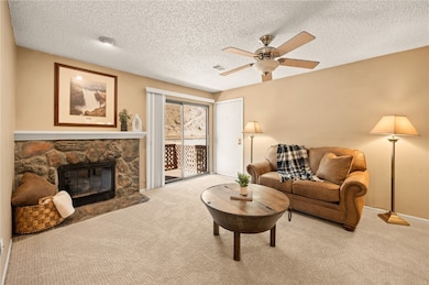 Carpeted living area with a textured ceiling, a stone fireplace, and a ceiling fan