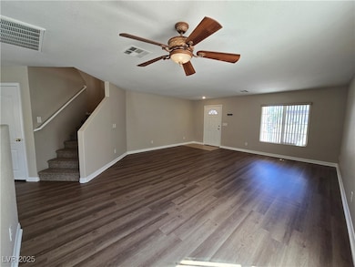 Unfurnished living room with stairs, dark wood-style flooring, and ceiling fan