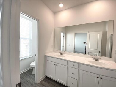 Bathroom featuring toilet, double vanity, baseboards, and wood finished floors
