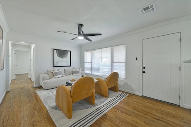 Living area featuring ornamental molding, light wood finished floors, a ceiling fan, baseboards, and a textured ceiling