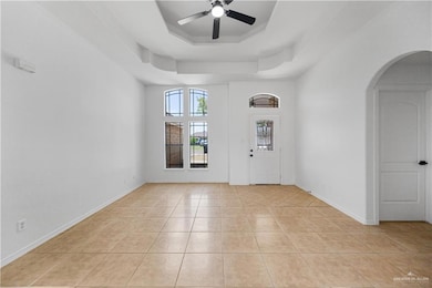 Entryway featuring a tray ceiling, light tile patterned floors, ceiling fan, arched walkways, and a towering ceiling