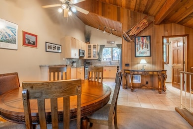 Dining area with light tile patterned floors, a wood ceiling with exposed beams, high vaulted ceiling, and ceiling fan