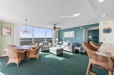 Carpeted living room featuring crown molding, ceiling fan with notable  Virtually edited imagechandelier, and expansive windows