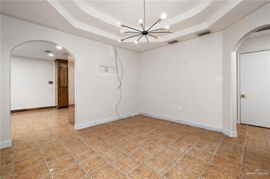 Empty room featuring a raised ceiling, arched walkways, and tile patterned floors