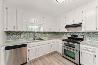 Kitchen with appliances with stainless steel finishes, under cabinet range hood, a sink, white cabinetry, and light wood-type flooring
