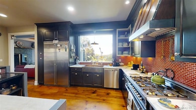 Kitchen with stainless steel appliances, open shelves, under cabinet range hood, decorative backsplash, and light wood-style flooring