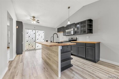 Kitchen featuring wood counters, open shelves, vaulted ceiling, a kitchen island with sink, and pendant lighting
