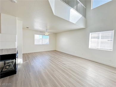 Unfurnished living room featuring a fireplace, plenty of natural light, light wood-type flooring, a textured ceiling, and a ceiling fan