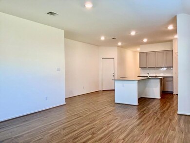 Kitchen with gray cabinetry, dark countertops, dark wood-type flooring, backsplash, and a center island with sink