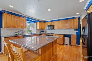 Kitchen featuring black appliances, a textured ceiling, light wood-style floors, brown cabinetry, and a kitchen island