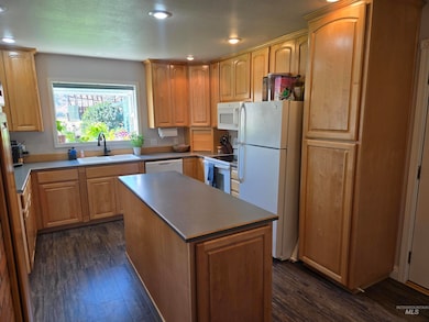 Kitchen featuring white appliances, dark wood finished floors, recessed lighting, a center island, and light brown cabinetry