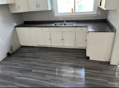 Kitchen with dark hardwood flooring, dark countertops, and white cabinetry