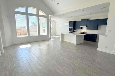 Kitchen with light countertops, a kitchen island with sink, tasteful backsplash, light wood-style flooring, and high vaulted ceiling