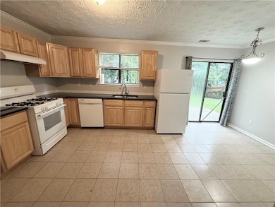 Kitchen with white appliances, under cabinet range hood, dark countertops, light tile patterned floors, and crown molding