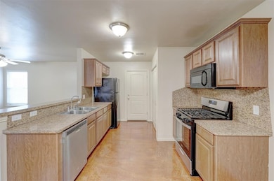 Kitchen featuring light brown cabinets, black appliances, ceiling fan, decorative backsplash, and light countertops