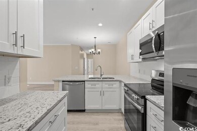 Kitchen with appliances with stainless steel finishes, a sink, a peninsula, a chandelier, and light wood-style floors