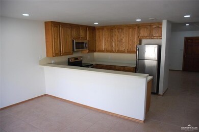 Kitchen with a peninsula, appliances with stainless steel finishes, brown cabinetry, light countertops, and recessed lighting