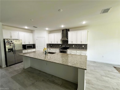 Kitchen with stainless steel appliances, wall chimney exhaust hood, a kitchen island with sink, white cabinetry, and backsplash