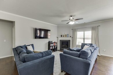 Living area with dark wood finished floors, crown molding, a ceiling fan, and a glass covered fireplace