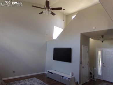 Living area with a towering ceiling, dark wood-type flooring, and a ceiling fan