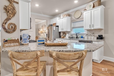 Kitchen featuring light hardwood / wood-style flooring, stainless steel appliances, a kitchen breakfast bar, kitchen peninsula, and light stone countertops