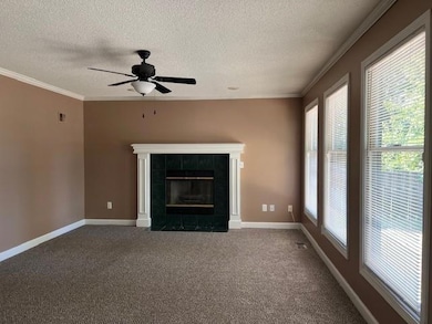 Unfurnished living room with a textured ceiling, a tiled fireplace, carpet flooring, ornamental molding, and a ceiling fan