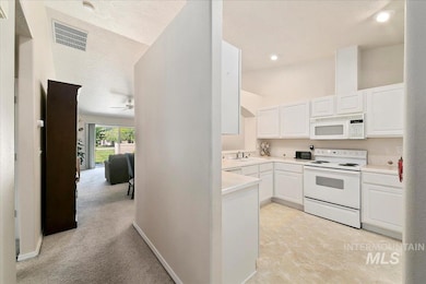 Kitchen with white appliances, white cabinetry, a textured ceiling, light countertops, and ceiling fan