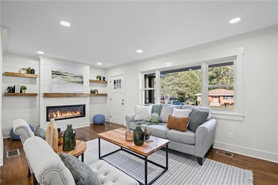 Living area with dark wood-style flooring, a glass covered fireplace, recessed lighting, and built in shelves