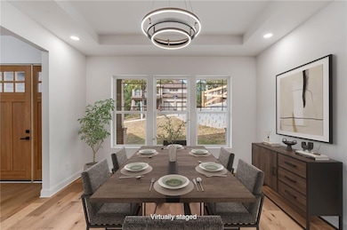 Dining area with light wood-style floors, a tray ceiling, recessed lighting, and a chandelier