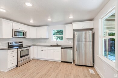 Kitchen with appliances with stainless steel finishes, light wood-style flooring, white cabinets, recessed lighting, and tasteful backsplash