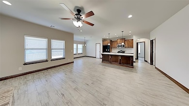 Kitchen featuring appliances with stainless steel finishes, open floor plan, light countertops, arched walkways, and baseboards