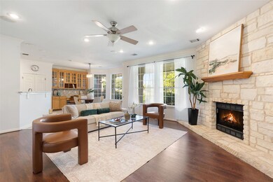 Sleek wood flooring, crown molding, and a charming floor-to-ceiling stone-built fireplace grace the airy living room.