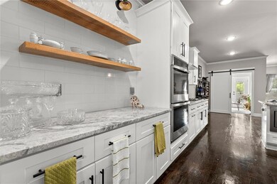 Kitchen featuring decorative backsplash, light stone countertops, open shelves, white cabinets, and a barn door