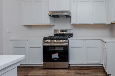 Kitchen with under cabinet range hood, stainless steel range with gas stovetop, light countertops, and white cabinets