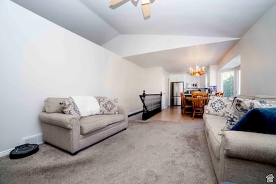 Living room with carpet floors, lofted ceiling, a chandelier, a ceiling fan, and tile patterned floors