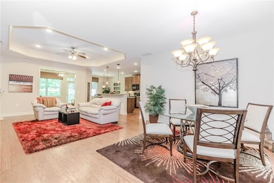 Dining room featuring a raised ceiling, a chandelier, light wood-style flooring, crown molding, and recessed lighting