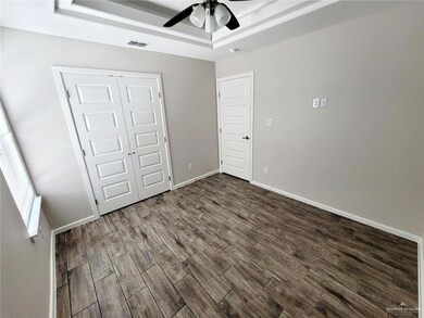 Unfurnished bedroom featuring dark wood-style flooring, a closet, ceiling fan, and a tray ceiling