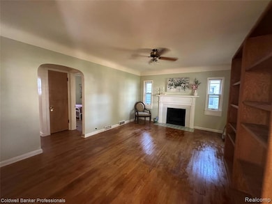 Unfurnished living room featuring dark wood-type flooring, arched walkways, a fireplace with flush hearth, and a ceiling fan