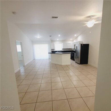 Kitchen with stainless steel fridge, light tile patterned floors, open floor plan, dark countertops, and recessed lighting