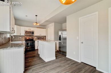 Kitchen featuring tasteful backsplash, appliances with stainless steel finishes, white cabinetry, a kitchen island, and light stone counters