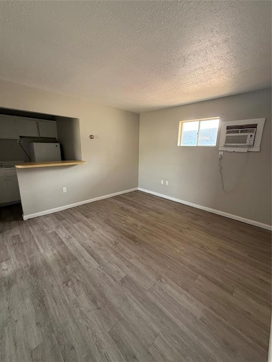 Unfurnished living room featuring wood finished floors, a textured ceiling, and a wall mounted air conditioner