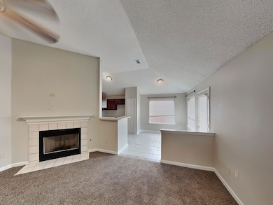 Unfurnished living room featuring light carpet, a textured ceiling, a tiled fireplace, vaulted ceiling, and light tile patterned floors